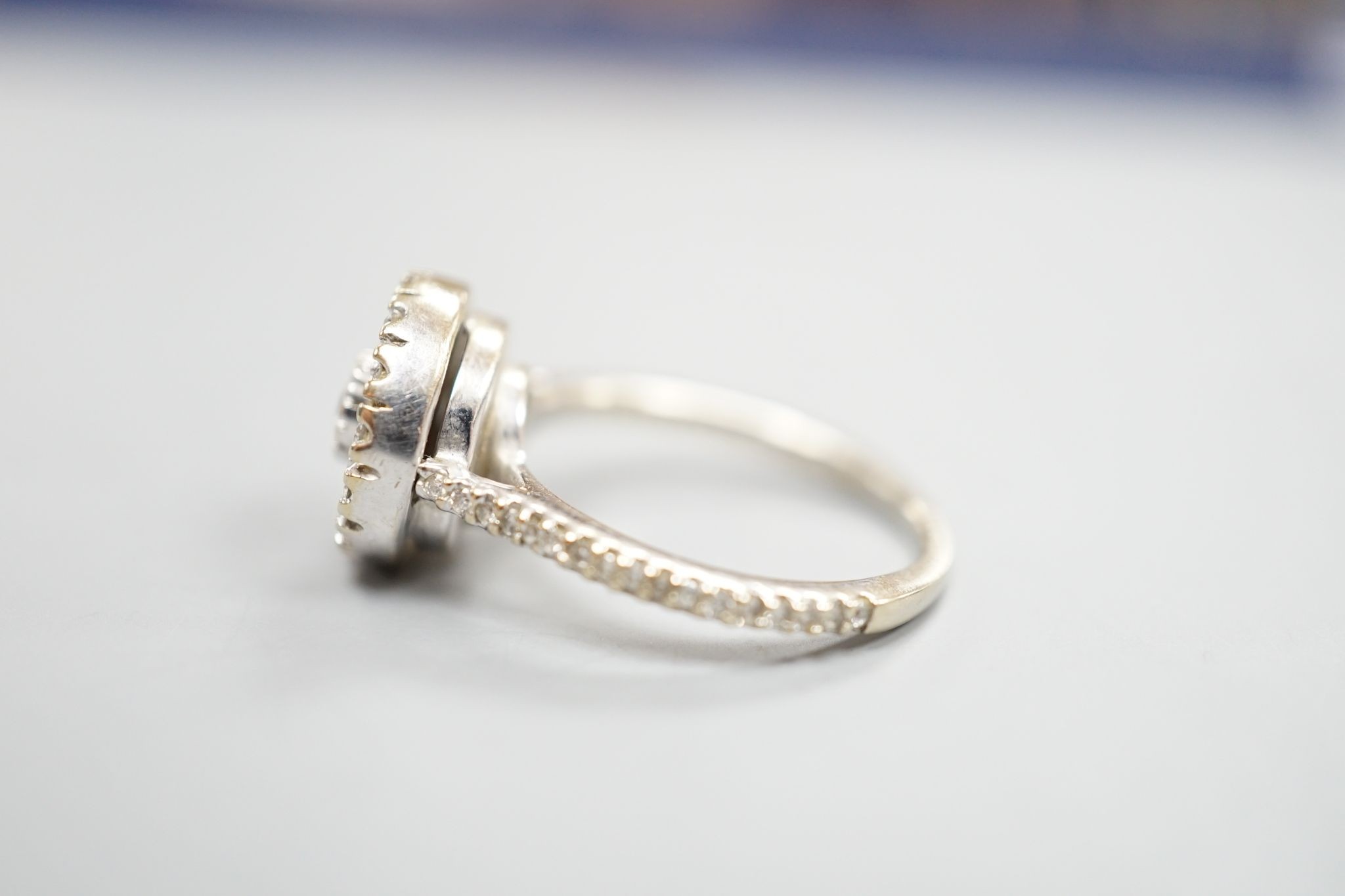 A modern white metal, round and trapeze cut diamond set target cluster ring, with diamond set shoulders, size N, gross weight 4.2 grams.